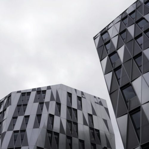 bottom-view-of-modern-unique-building-with-triangle-shaped-windows-of-black-color-on-bright-cloudy-e1695971005517.jpg